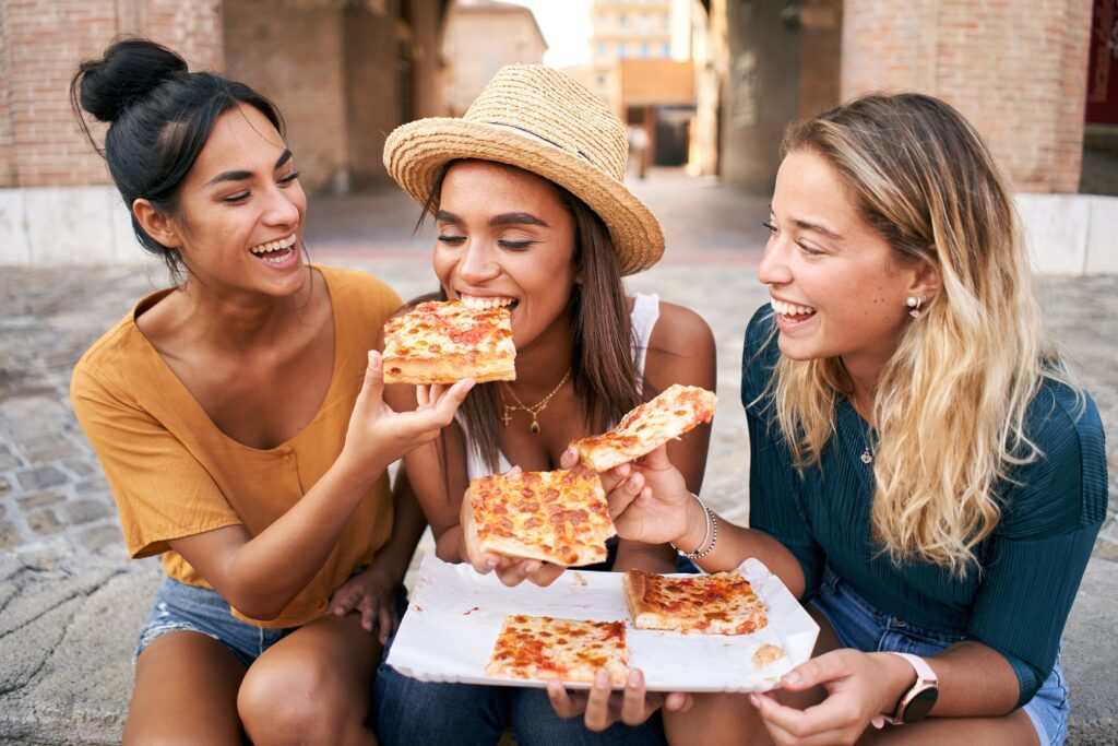 Funny group of three girls and they have fun eating pizza in the touristic city. Italian woman having street food. High quality photo