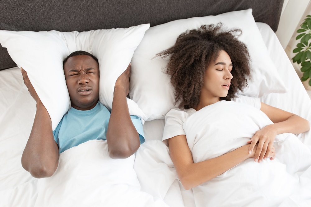 Insomnia from snoring, interfere with sleep and health problems. Millennial african american female sleeping and snoring, sad male suffers and covers his ears with pillow, empty space, top view